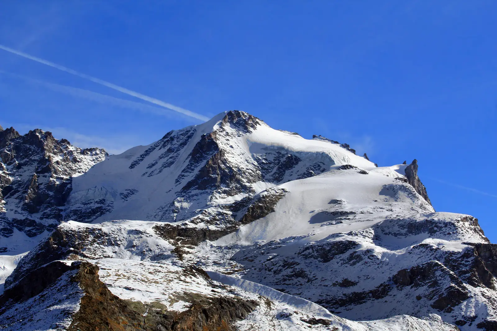 Gran Paradiso from the west: a snow summit and glaciers above dark rocky ridges, under a clear sky.