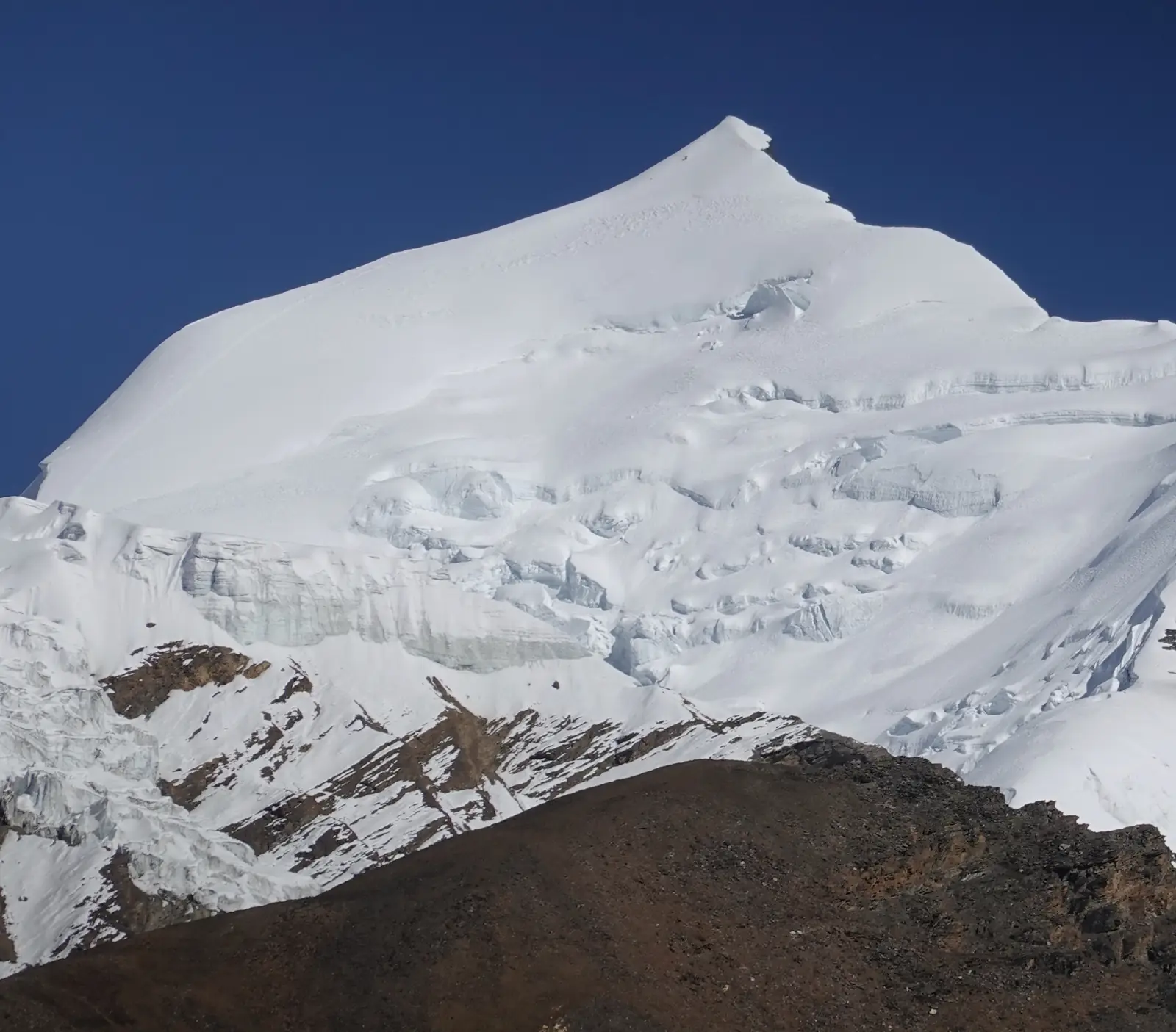 The snow pyramid of Himlung Himal above a broken icefall, seen from base camp against a dark blue sky.
