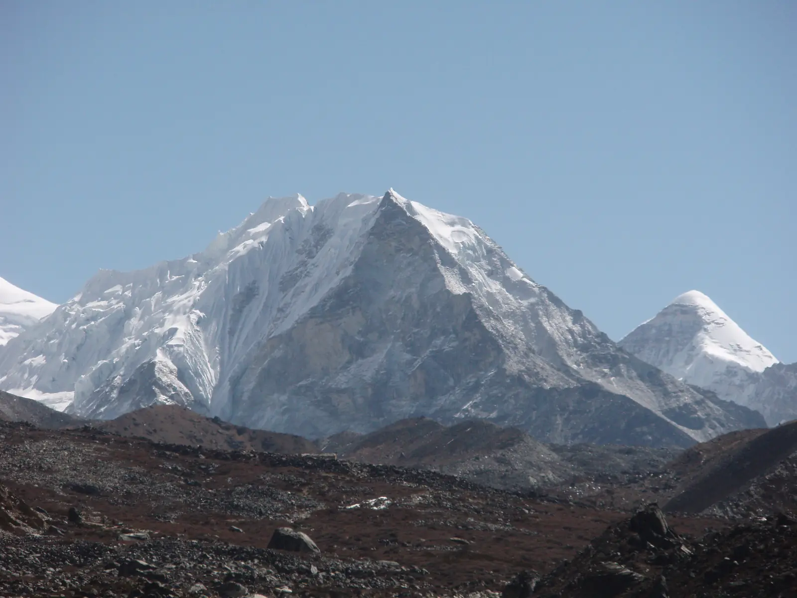 The snow-streaked rock pyramid of Island Peak above a stony moraine, with a smaller white peak to its right.