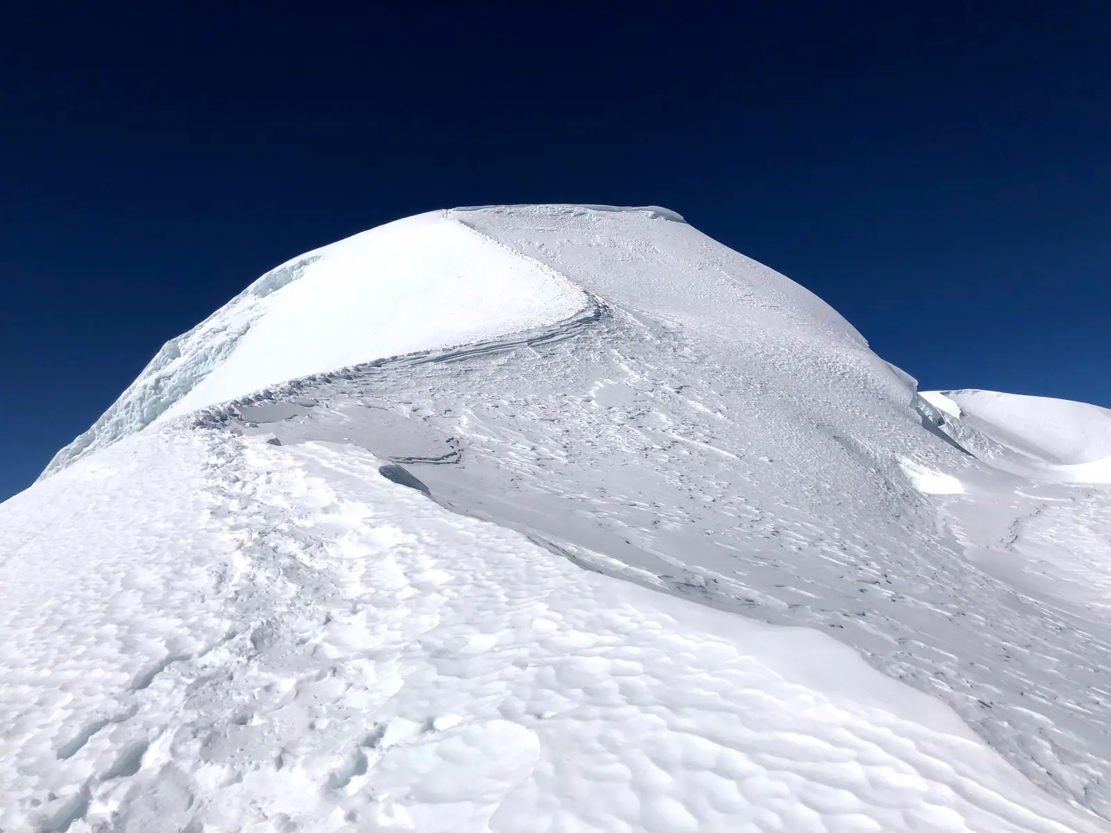 The rounded snow dome at the top of Mera Peak against a dark blue sky, seen from the upper glacier.