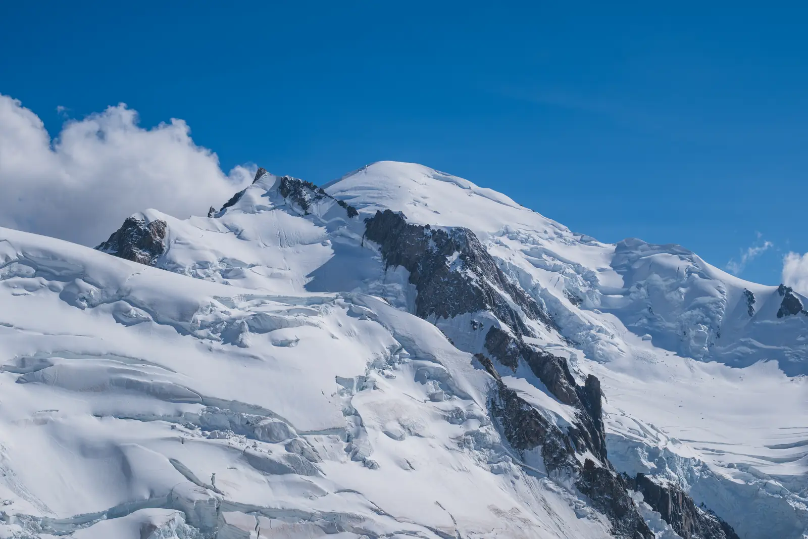 Mont Blanc’s rounded summit dome and the rocky top of Mont Maudit above broken, crevassed glaciers.