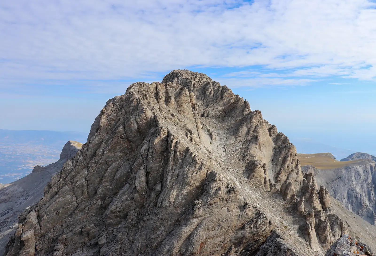 Mytikas, the summit of Olympus: a pyramid of grey limestone ribs and gullies against a hazy sky.